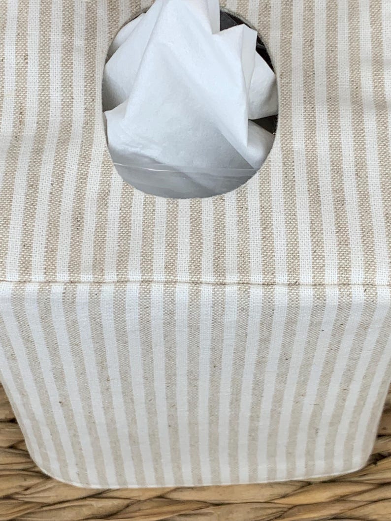 Peut inclure: Une housse de bo&icirc;te &agrave; mouchoirs rectangulaire avec un motif &agrave; rayures verticales beige et blanc cass&eacute;. La housse pr&eacute;sente une ouverture ovale centr&eacute;e sur le dessus, laissant appara&icirc;tre un mouchoir blanc. Le tissu a un aspect tiss&eacute; textur&eacute;.