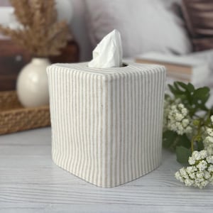 Peut inclure: Une housse de bo&icirc;te &agrave; mouchoirs carr&eacute;e en tissu avec un motif &agrave; rayures verticales beige et blanc cass&eacute;. La housse est con&ccedil;ue pour recouvrir une bo&icirc;te &agrave; mouchoirs carr&eacute;e standard, avec un mouchoir blanc d&eacute;passant de l'ouverture sup&eacute;rieure.