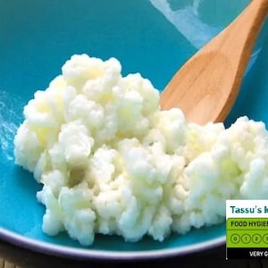May include: A turquoise bowl filled with white kefir grains, with a wooden spoon resting inside. The image includes a food hygiene rating of 5, labeled "Very Good", and the text "Tassu's kefir".