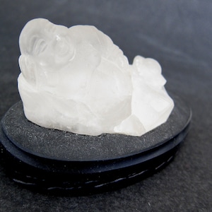 May include: A white crystal sculpture of a sleeping Buddha on a black base.