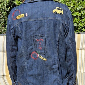 May include: Dark blue denim jacket with embroidered school-themed patches. Features an apple and pencil, a yellow school bus, and the phrase "Teaching is a Joy".