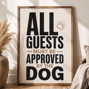Könnte beinhalten: Gerahmtes Wandbild mit dem Text "ALL GUESTS MUST BE APPROVED BY THE DOG" in Schwarz und Braun. Ein Pfotenabdruck befindet sich über dem Text. Der Rahmen ist hellbraun.