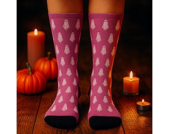 May include: Pink socks with a repeating white ghost pattern. The socks have black toes and cuffs. The image is set against a dark background with pumpkins and lit candles, creating a Halloween theme.