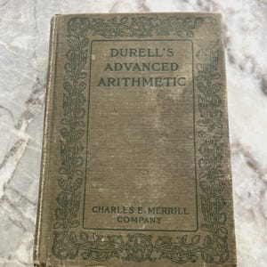 以下が含まれることがあります： 装飾的な縁取りのあるビンテージグリーンの書籍。タイトルは「Durell's Advanced Arithmetic」、出版社は「Charles E. Merrill Company」です。
