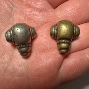 May include: Two small, antique metal knobs. One is silver-toned, the other is gold-toned. Each knob has a rounded top with horizontal ridges and a tapered, ribbed base. The knobs are likely for furniture or decorative use.