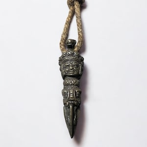 May include: A bronze pendant with a detailed face and a pointed tip, hanging from a brown cord.