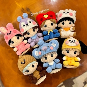 May include: A collection of handmade crochet dolls, each featuring a unique character design. The dolls are dressed in various outfits and hats, including a bunny, koala, and bear. The dolls are displayed on small wooden stands.