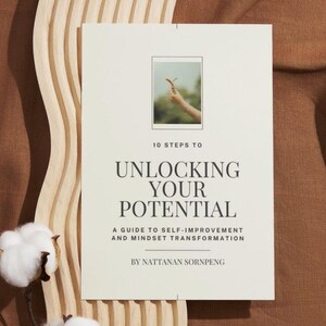 Puede incluir: Un libro blanco con el título "Unlocking Your Potential" en texto negro. El subtítulo es "A Guide to Self-Improvement and Mindset Transformation" y el autor es "Nattanana Sornpeng".