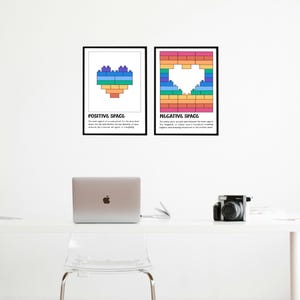 May include: Two framed art prints on a white wall. One print says "POSITIVE SPACE" and features a colorful heart made of blocks. The other print says "NEGATIVE SPACE" and shows a heart-shaped cutout in a block design.