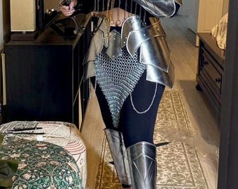 Könnte beinhalten: Ein silberner Metall-Rüstungsset mit Kettenhemd-Akzenten. Die Rüstung umfasst ein Bruststück, Schulterpolster, einen Rock und Beinschützer. Die Rüstung wird über einer schwarzen Leggings getragen.