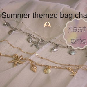 May include: Summer themed bag chains with seashell and starfish charms in gold and silver tones. The chains are displayed on a soft, white fabric. The image includes the text "last one".