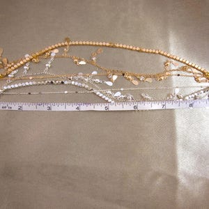 May include: Two decorative chain straps with lobster claw clasps at each end. One strap is gold-toned with dangling teardrop charms, and the other is silver-toned with flat circular discs. A white measuring tape shows a length of 10 inches.