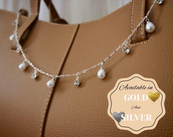 May include: A silver-toned chain necklace featuring alternating teardrop-shaped white faux pearls and clear round crystals. A beige graphic badge in the corner displays the text: Available in GOLD And SILVER with heart icons.