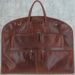 May include: A brown leather garment bag with multiple pockets and a zipper closure. The bag has a handle and a tag that says "Leather".