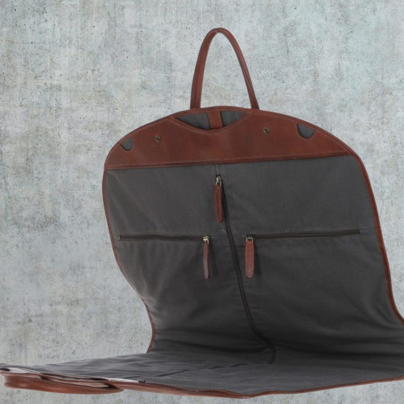K&ouml;nnte beinhalten: Eine braune Leder-Kleidertasche mit grauem Futter und mehreren Taschen. Die Tasche ist offen und das Futter ist sichtbar. Die Tasche hat einen Griff oben.