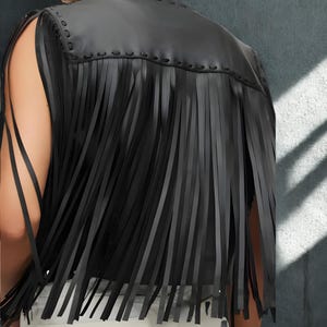 K&ouml;nnte beinhalten: Schwarze Lederweste mit langen Fransen. Die Weste hat ein &auml;rmelloses Design und einen gen&auml;hten Ausschnitt. Die Fransen h&auml;ngen vertikal und erzeugen einen geschichteten Effekt. Die Weste ist einfarbig schwarz.