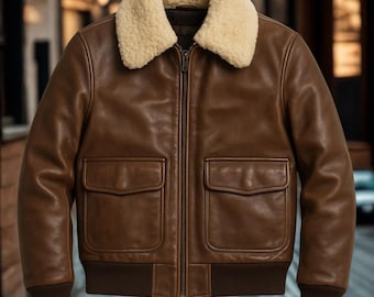 May include: Brown leather jacket with a cream-colored shearling collar. The jacket features a zip-up front, two front pockets, and ribbed cuffs and hem. A classic outerwear piece.