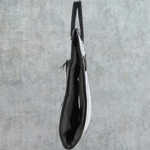 May include: A black leather tote bag with a zipper closure and a top handle. The bag is folded in half and standing upright.