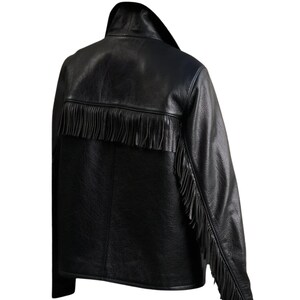 May include: Black leather jacket with fringe detailing across the back and down the sleeves. The jacket has a classic collar and a textured appearance, offering a stylish, edgy look. A fashionable outerwear piece.