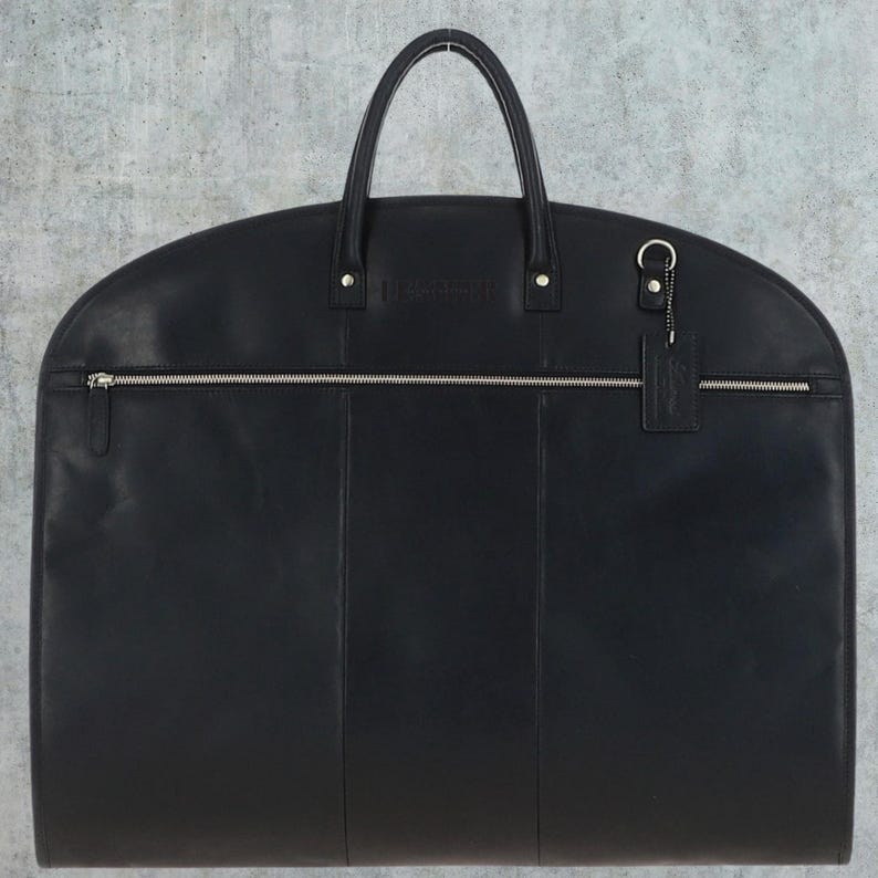 May include: Black leather garment bag with a zippered pocket and a small leather tag with the word "Travelpro" embossed on it.