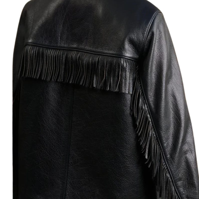 May include: Black leather jacket with fringe detail across the upper back and down the sleeves. The jacket has a classic design with a textured finish, offering a stylish and edgy look. The fringe adds a unique, decorative element.