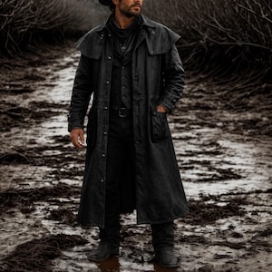May include: A long, black, heavy-duty duster coat featuring a shoulder cape, a button-front closure, and large patch pockets. The coat is worn over a matching black vest and dark trousers, creating a monochromatic, full-length outer garment.