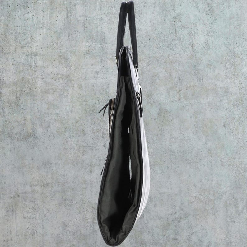 K&ouml;nnte beinhalten: Eine schwarze Ledertasche mit Rei&szlig;verschluss und einem oberen Henkel. Die Tasche ist in der Mitte gefaltet und steht aufrecht.