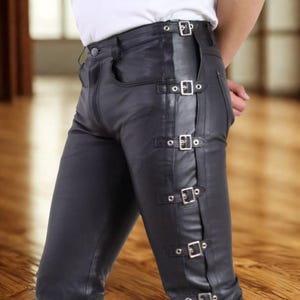 May include: Black leather pants with silver buckles along the side. The pants have a classic five-pocket design and a button closure. The leather appears smooth and has a slight sheen. The pants are tailored for a close fit.