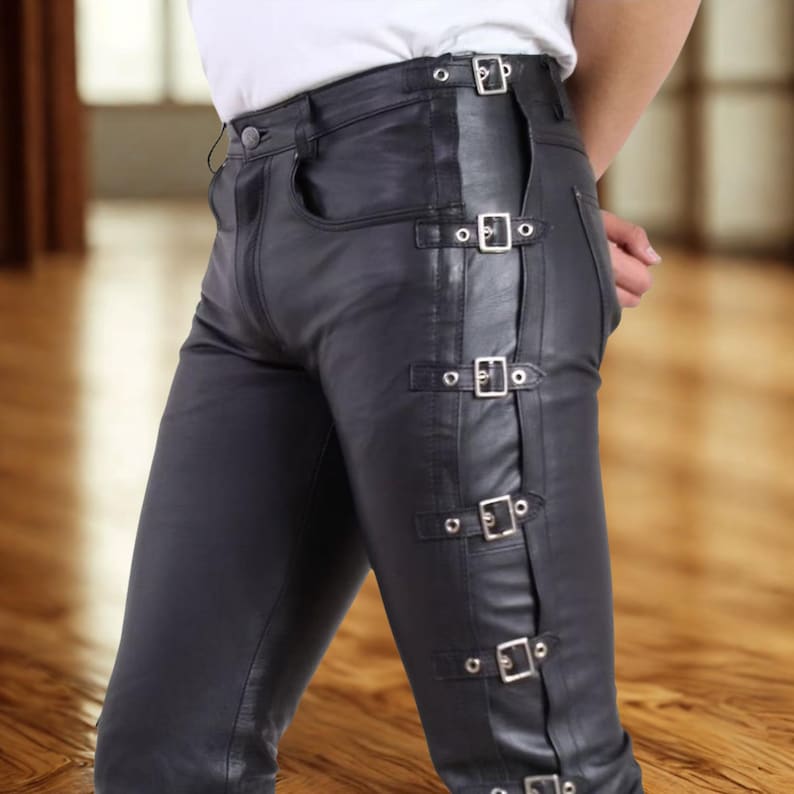 May include: Black leather pants with silver buckles along the side. The pants have a classic five-pocket design and a button closure. The leather appears smooth and has a slight sheen. The pants are tailored for a close fit.