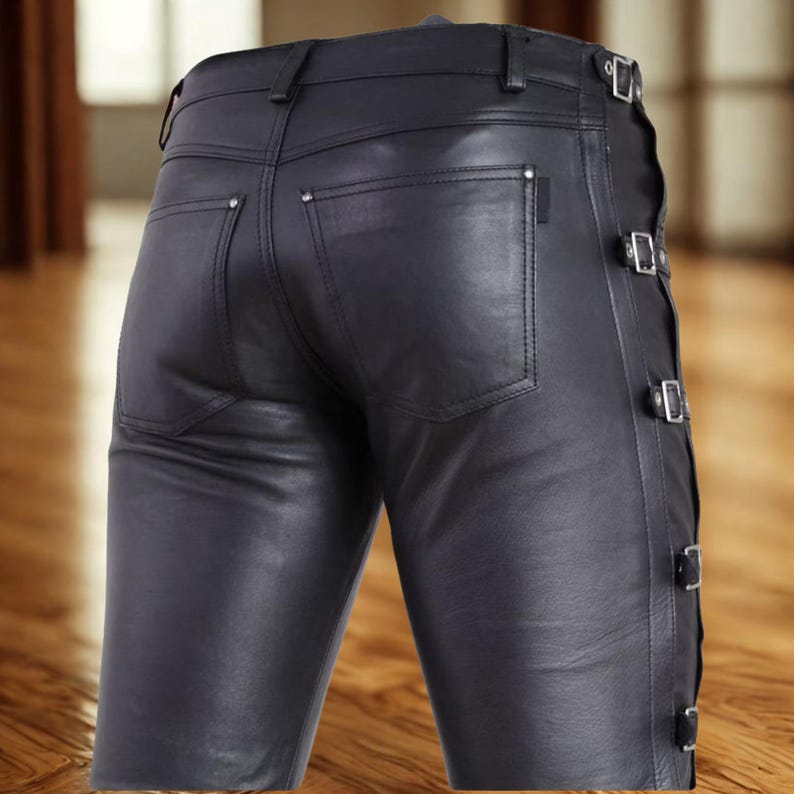 May include: Black leather pants with a classic five-pocket design. The pants feature decorative silver rivets and adjustable side straps with buckles. The leather has a slight sheen, and the pants appear to be tailored for a close fit.