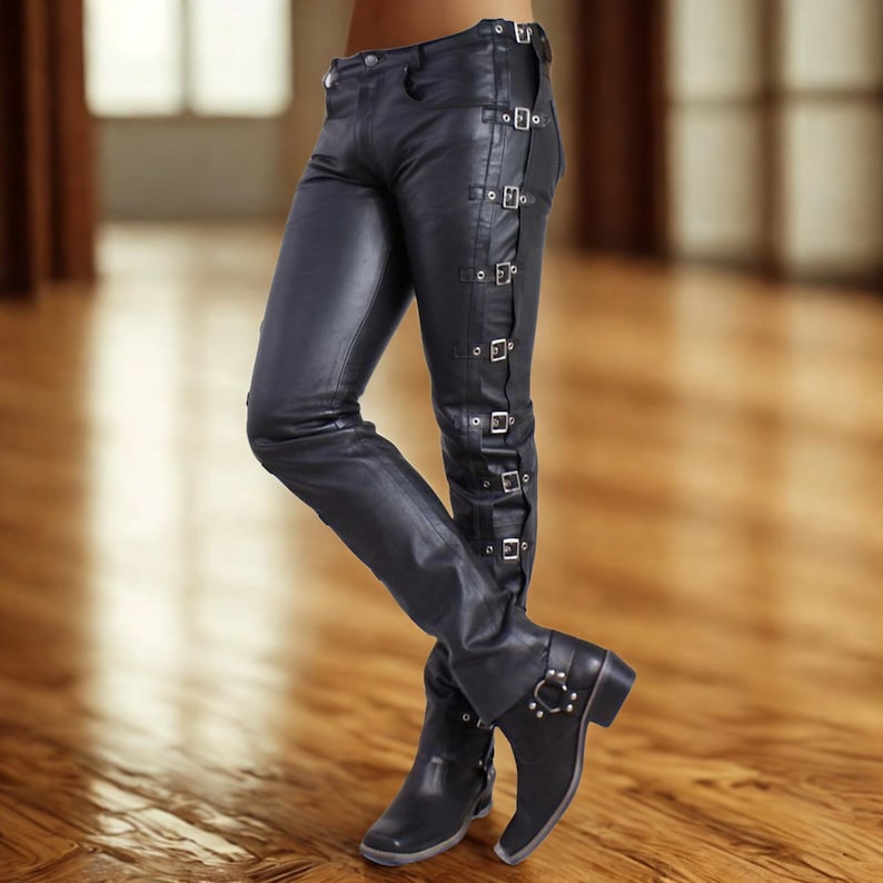 May include: Black leather pants with multiple silver buckles running down the side of each leg. The pants are paired with black boots featuring a silver buckle detail. The pants have a fitted design.