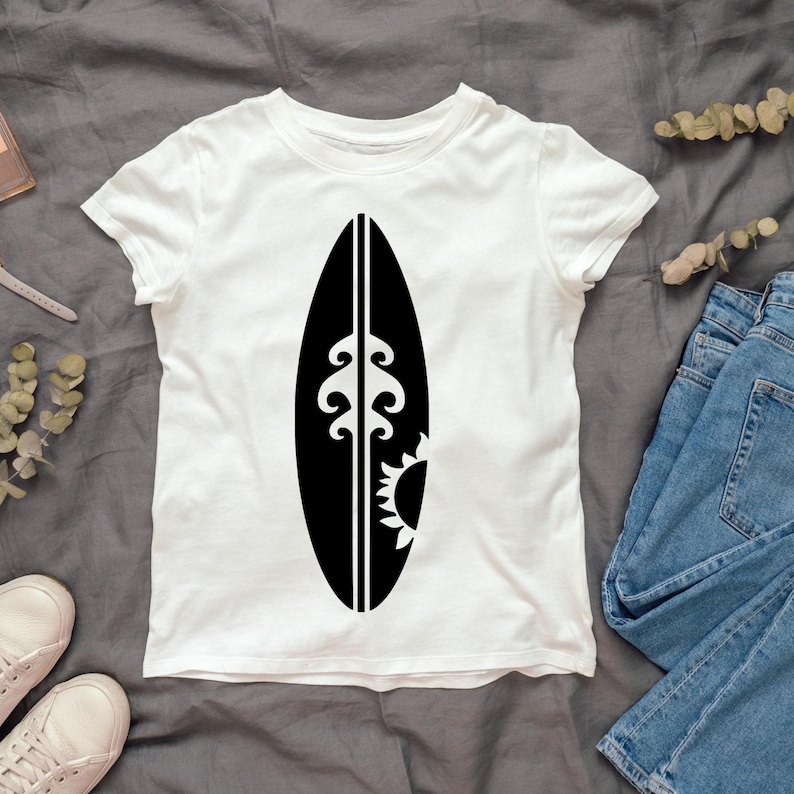 May include: White t-shirt with a black graphic of a surfboard with a wave and sun design.