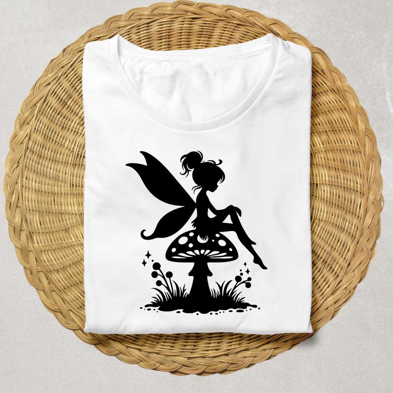 Op de afbeelding: Wit T-shirt met een zwart silhouet van een fee die op een paddenstoel zit.