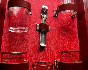 Przenośny, zabytkowy zestaw barowy składający się z sześciu szklanek i otwieracza do butelek.