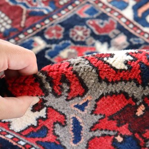 A close-up view of a hand holding a vibrant, intricately patterned rug with a mix of red, blue, and white colors.