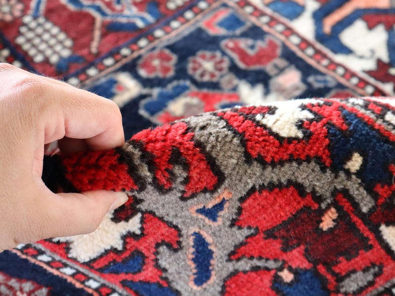A close-up view of a hand holding a vibrant, intricately patterned rug with a mix of red, blue, and white colors.