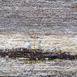 The image is a close-up of a carpet with a detailed pattern, featuring a small tree and two people in the center.