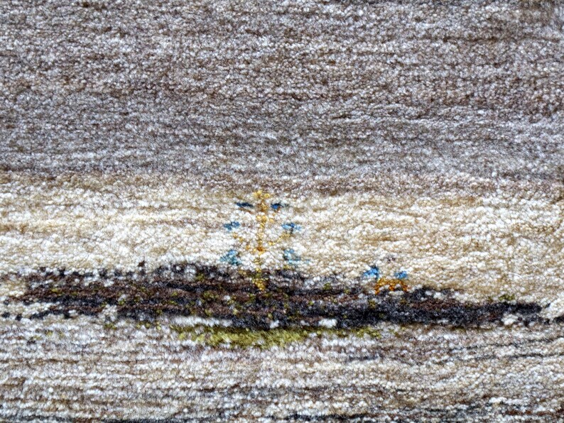 The image is a close-up of a carpet with a detailed pattern, featuring a small tree and two people in the center.