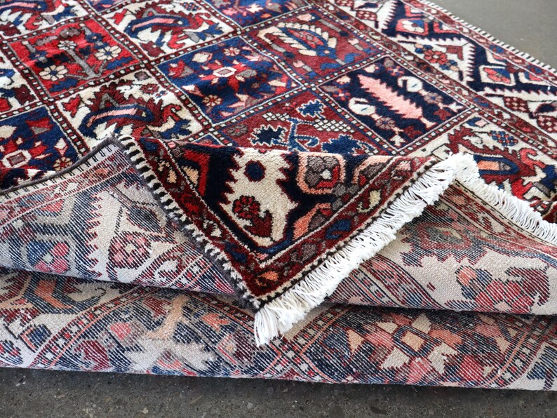 a close-up view of a colorful, intricately patterned rug with a mix of red, blue, and white colors. The rug has a fringe at the edges, adding to its decorative appearance. The rug appears to be folded or rolled up, revealing its detailed design.