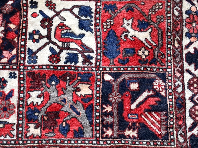 The image is a close-up of a vibrant, intricately designed rug with a variety of patterns and motifs. The rug features a mix of red, blue, and white colors, as well as various geometric shapes and figures, including animals, trees, and abstract designs. The overall composition of the image is visually striking and detailed, showcasing the craftsmanship and artistry involved in creating this textile.