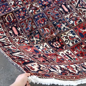 A hand is holding a colorful, intricately patterned rug with a variety of geometric shapes and designs.
