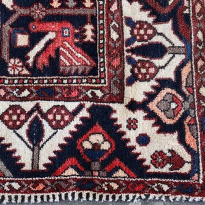a close-up view of a colorful, intricately patterned rug with a mix of red, blue, and white colors. The rug features various geometric shapes and designs, including flowers, leaves, and geometric patterns. The rug appears to be a traditional rug, with a fringe at the edge.