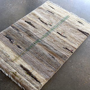 a rug with a geometric pattern of stripes and a green line running through it, placed on a concrete floor.