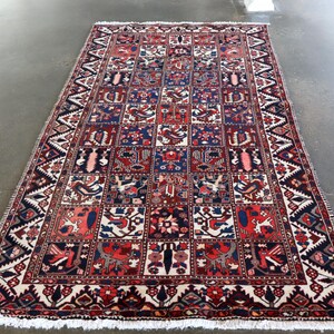 a large, intricately designed rug with a vibrant pattern of red, blue, and white colors. The rug is placed on a concrete floor, and the background is blurred, drawing attention to the rug itself.