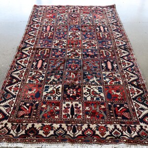 a large, intricately patterned rug with a variety of colors and designs, including geometric shapes and floral motifs. The rug is placed on a concrete floor, and there is a second rug visible in the background.