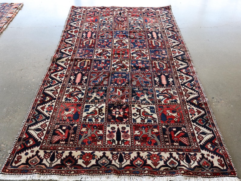 a large, intricately patterned rug with a variety of colors and designs, including geometric shapes and floral motifs. The rug is placed on a concrete floor, and there is a second rug visible in the background.