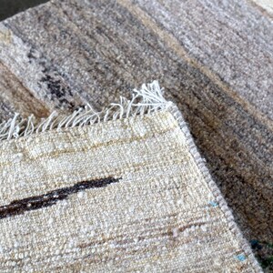 a close-up view of a textured fabric, possibly a rug or carpet, with a darker, more textured area in the background.