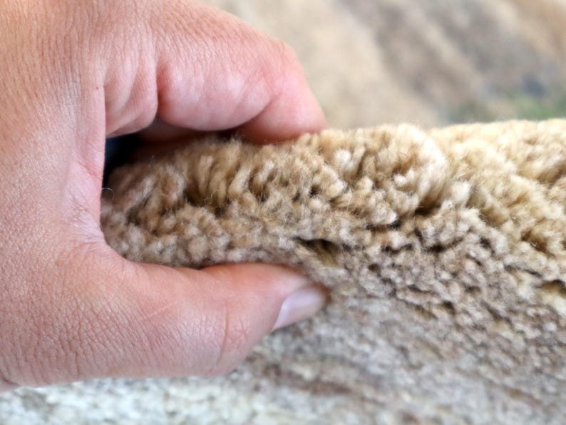 A close-up image of a hand holding a piece of beige carpet.