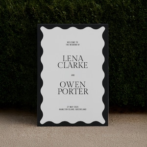 Minimal black and white wedding welcome sign with bold wavy border framed against hedge; elegant modern typography; editable Canva template sized for A1/A2 and 24×36/18×24; printable straight-edge design for ceremony or reception entry.
