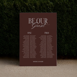 May include: A dark burgundy wedding seating chart with elegant script that reads "BE OUR Guest". The chart is divided into two columns, "ONE" and "TWO", each listing guest names. The phrase "YOUR SEAT AWAITS" is at the bottom.